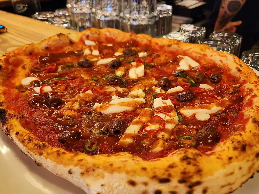 Freshly baked pizza with mozzarella, olives, and chili peppers on wooden counter