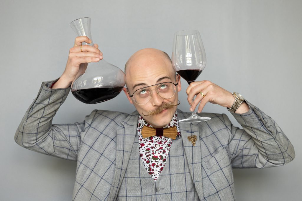 A sommelier handing a glass of red wine and a carafe of wine