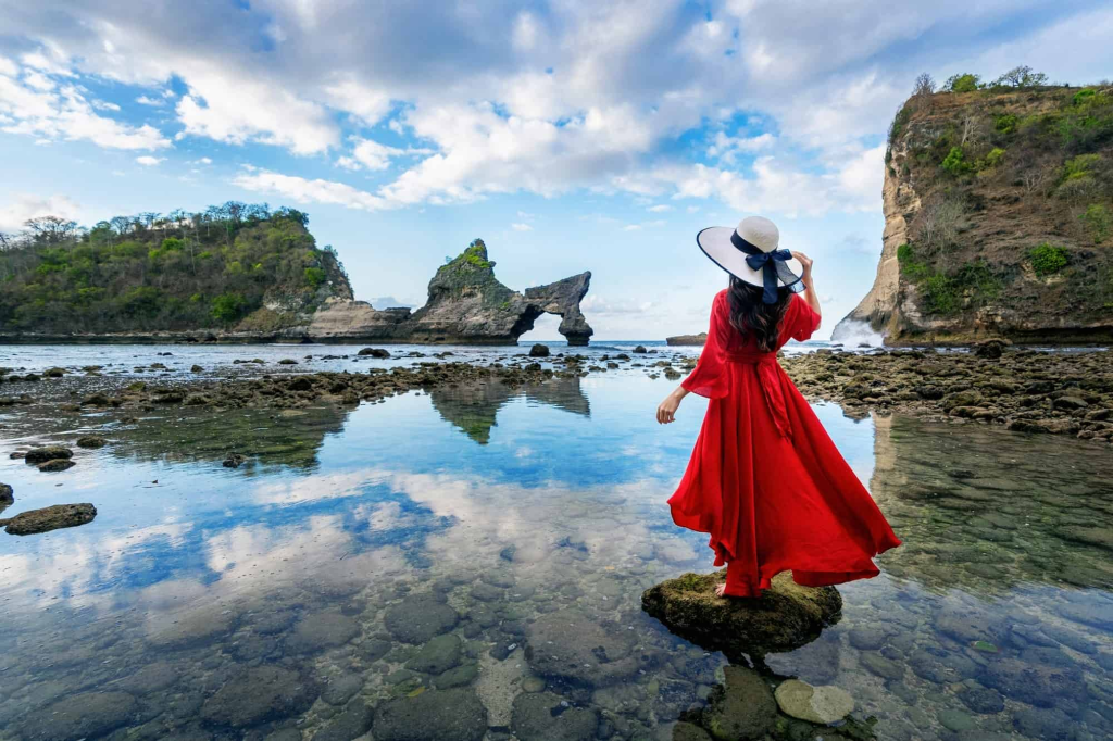 A woman in a red dress standing in the shallow ocean in Bali