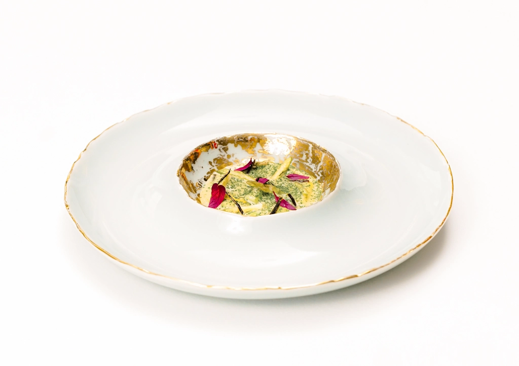 Artisanal creamy dish with green herbs in a gold-rimmed plate