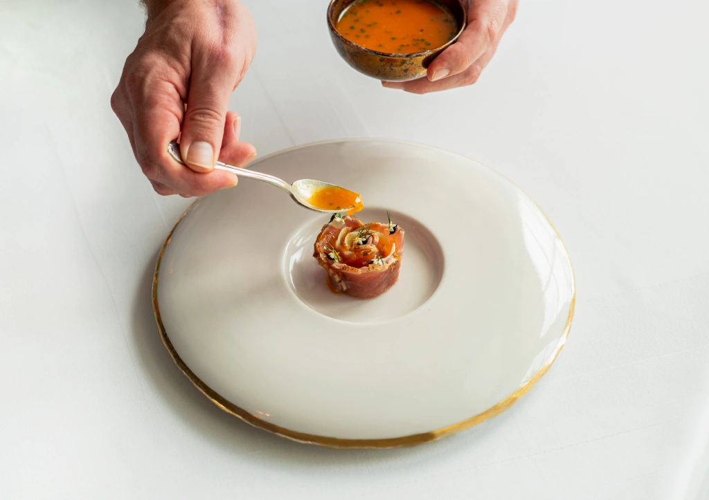 Chef pouring orange sauce onto a rose-shaped meat appetizer