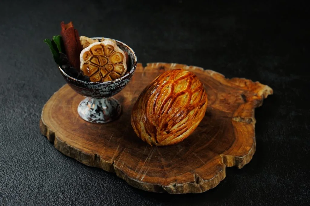Golden puff pastry served with roasted garlic on wooden board