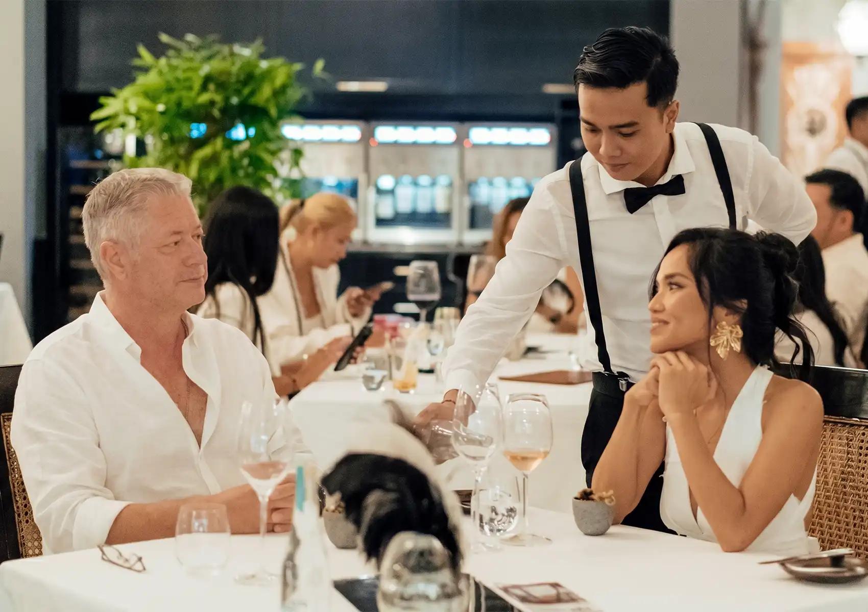 Elegant restaurant scene with waiter serving drinks to guests at white‑tablecloth table in refined dining atmosphere.