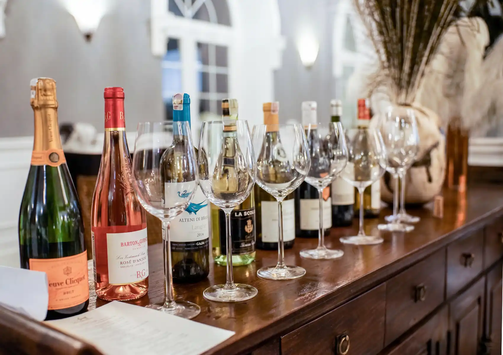 Wine tasting setup with sparkling, rosé, and white wine bottles arranged with glasses on elegant wooden counter.