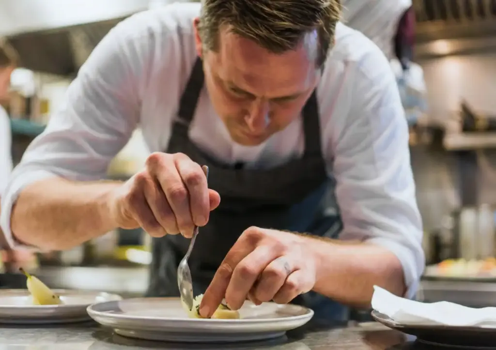 Belgian chef carefully plating a dish in a professional kitchen, fine dining Bali culinary craftsmanship
