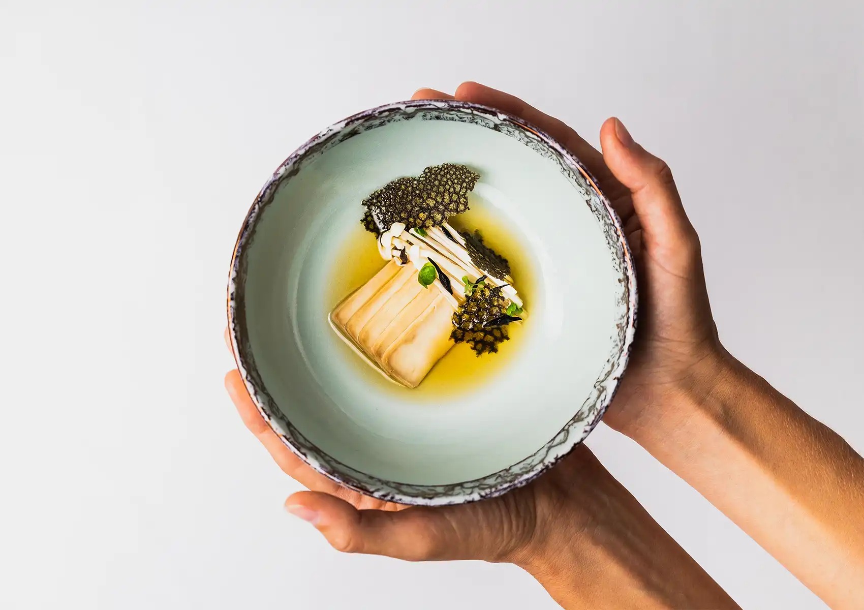 Chef presenting artfully plated dish with enoki mushrooms and crispy tuile in a ceramic bowl, fine dining Bali borderless cuisine concept