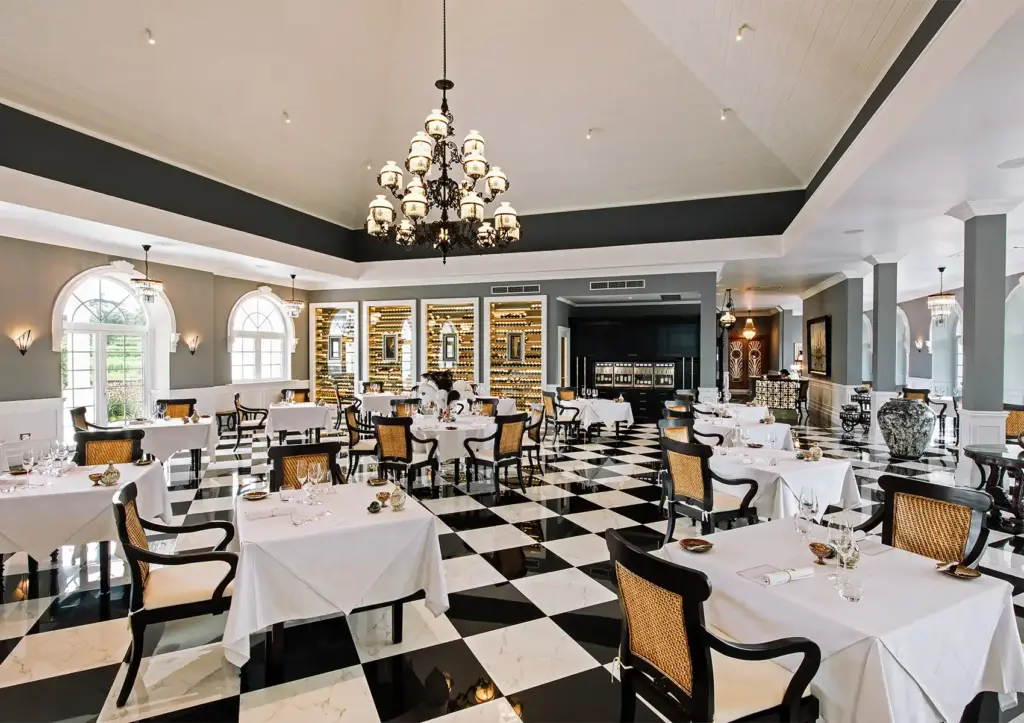 A luxurious restaurant interior featuring a striking black and white checkered floor, crisp white tablecloths, a grand chandelier, and an extensive wine cellar wall, showcasing the elegant atmosphere of fine dining Ubud.