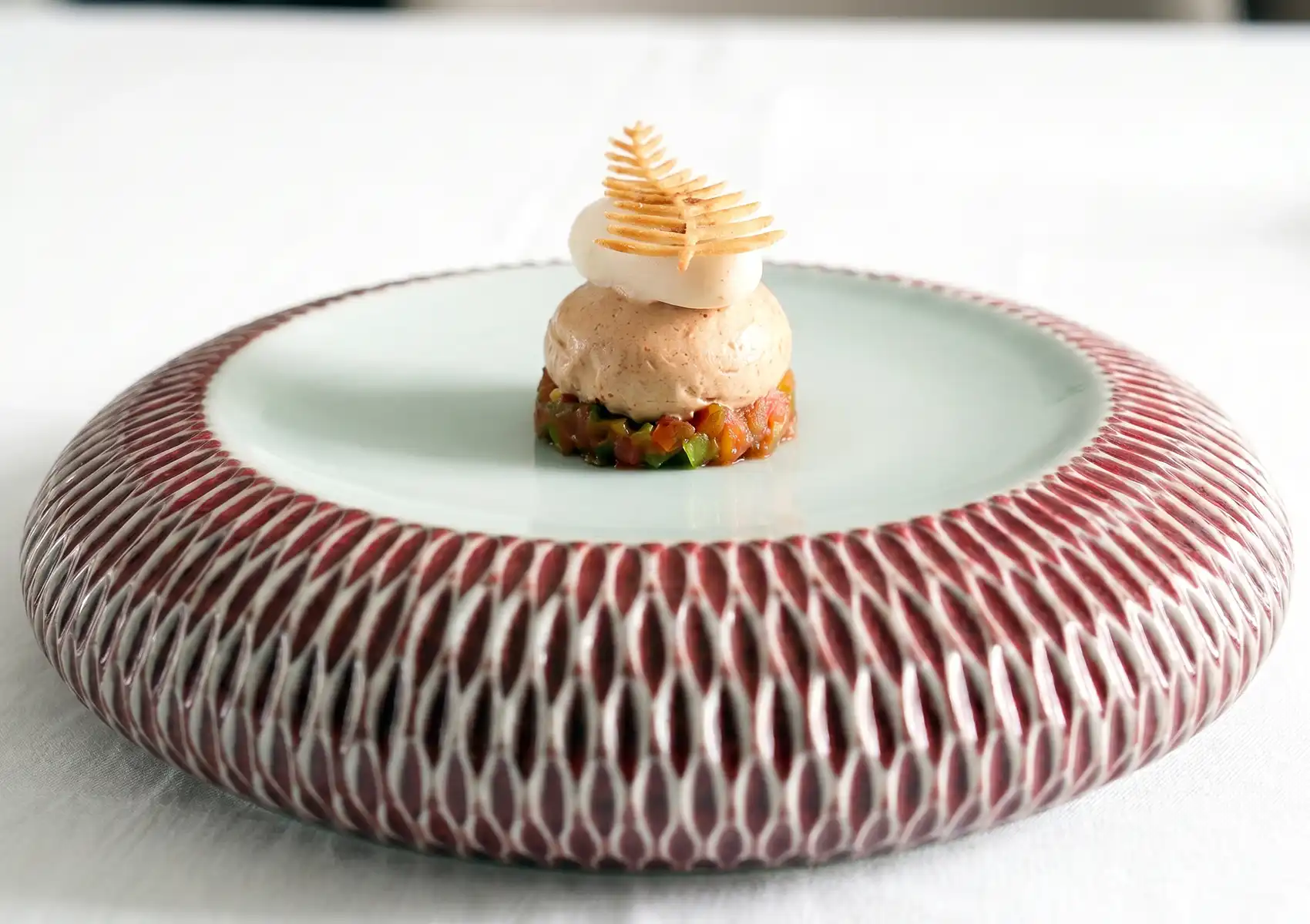 Close-up side view of a meticulously plated gourmet appetizer featuring a diced tomato base, a smooth spherical mousse, and a delicate leaf-shaped tuile, showcasing sustainable fine dining Ubud.