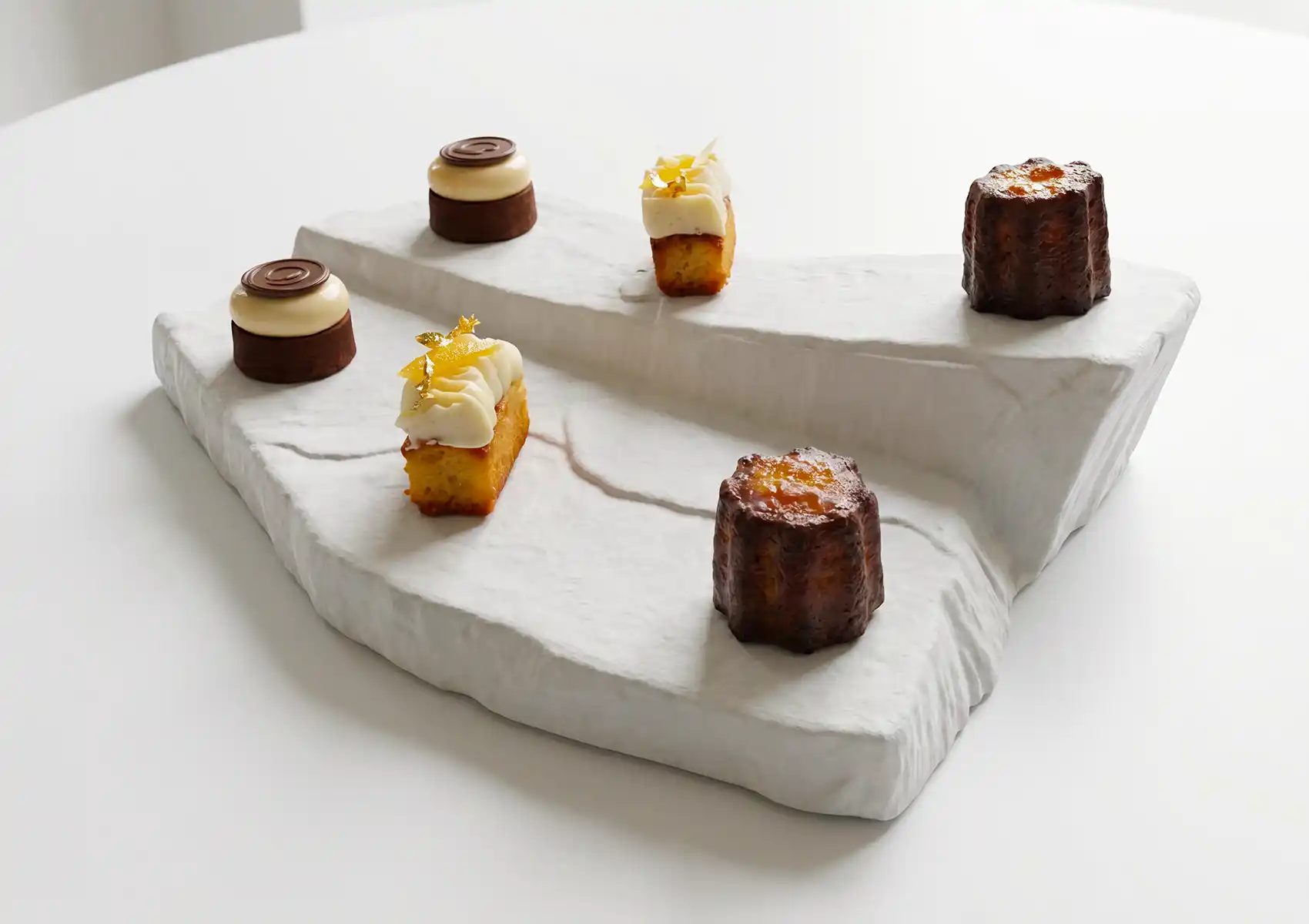 Assortment of petits fours including canelés and citrus cakes on a marble serving board, fine dining Bali dessert presentation