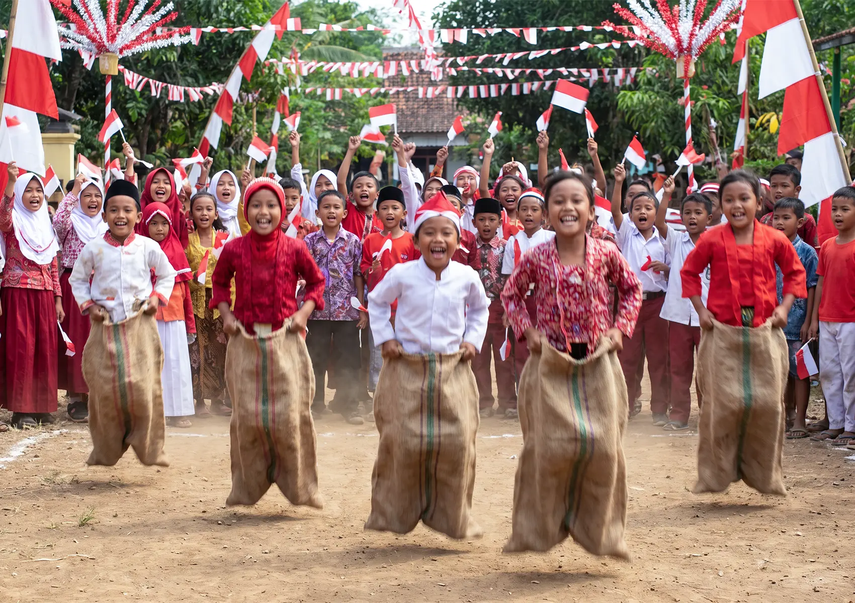 Joyful children participating in a traditional sack race and waving red and white flags in celebration of Indonesian Independence Day Bali.