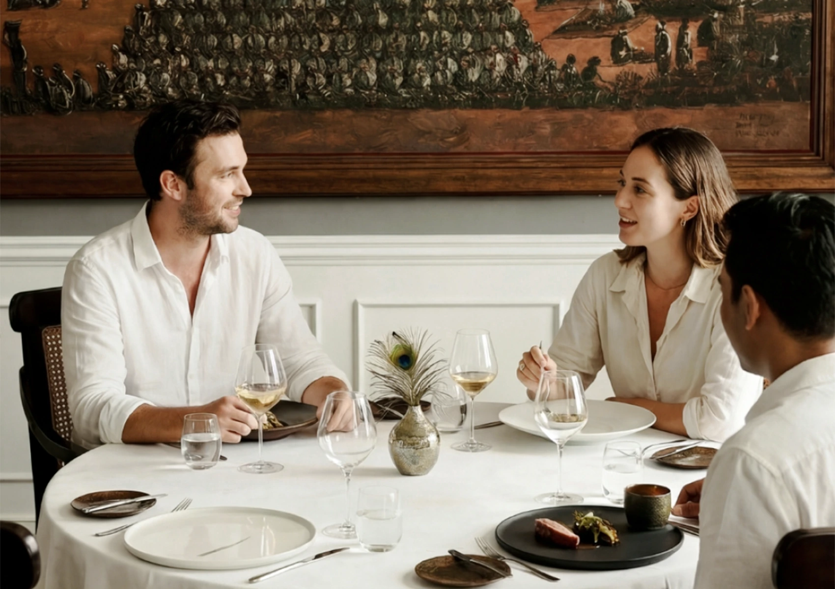 A group of friends conversing at an elegant restaurant table, demonstrating an appropriate fine dining dress code Bali with their crisp, smart-casual white shirts.