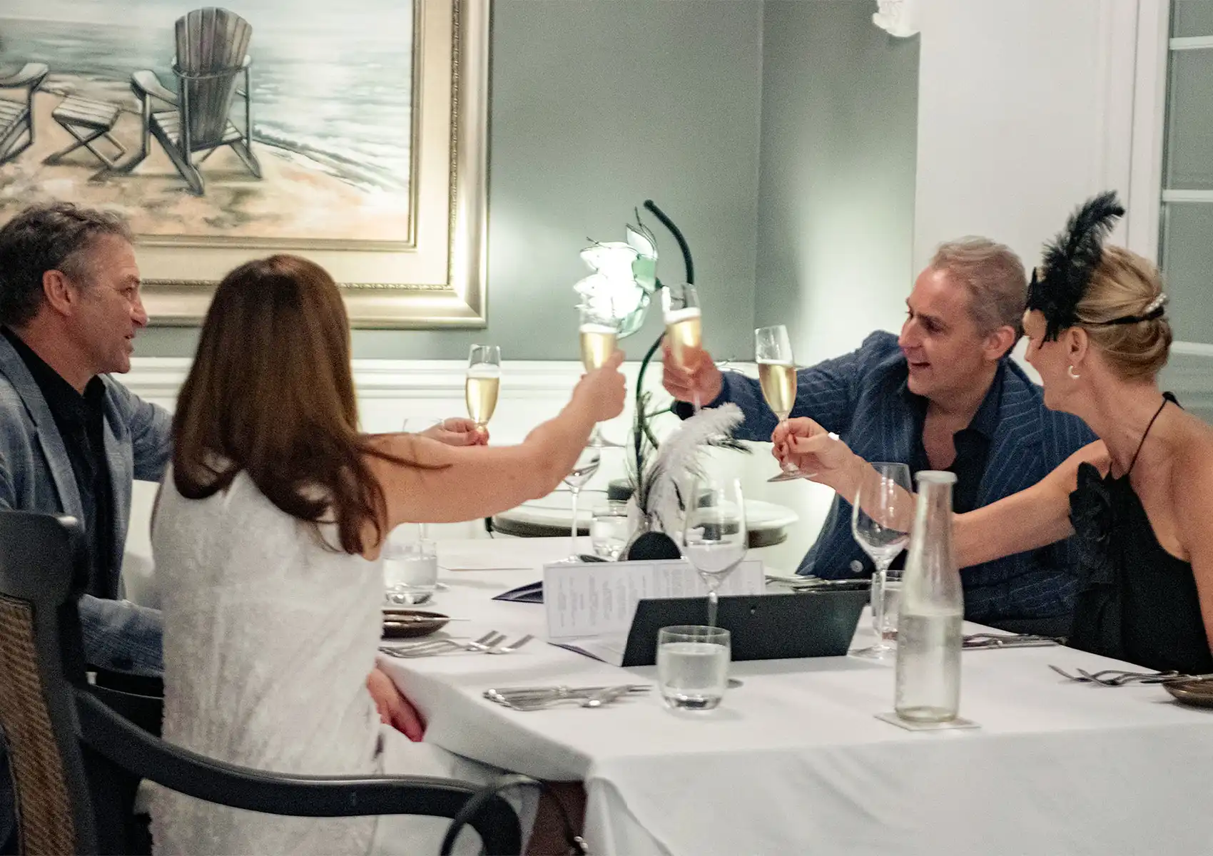 Two smartly dressed couples smiling and toasting with champagne glasses at a beautifully set table, enjoying a celebratory evening of fine dining ubud.