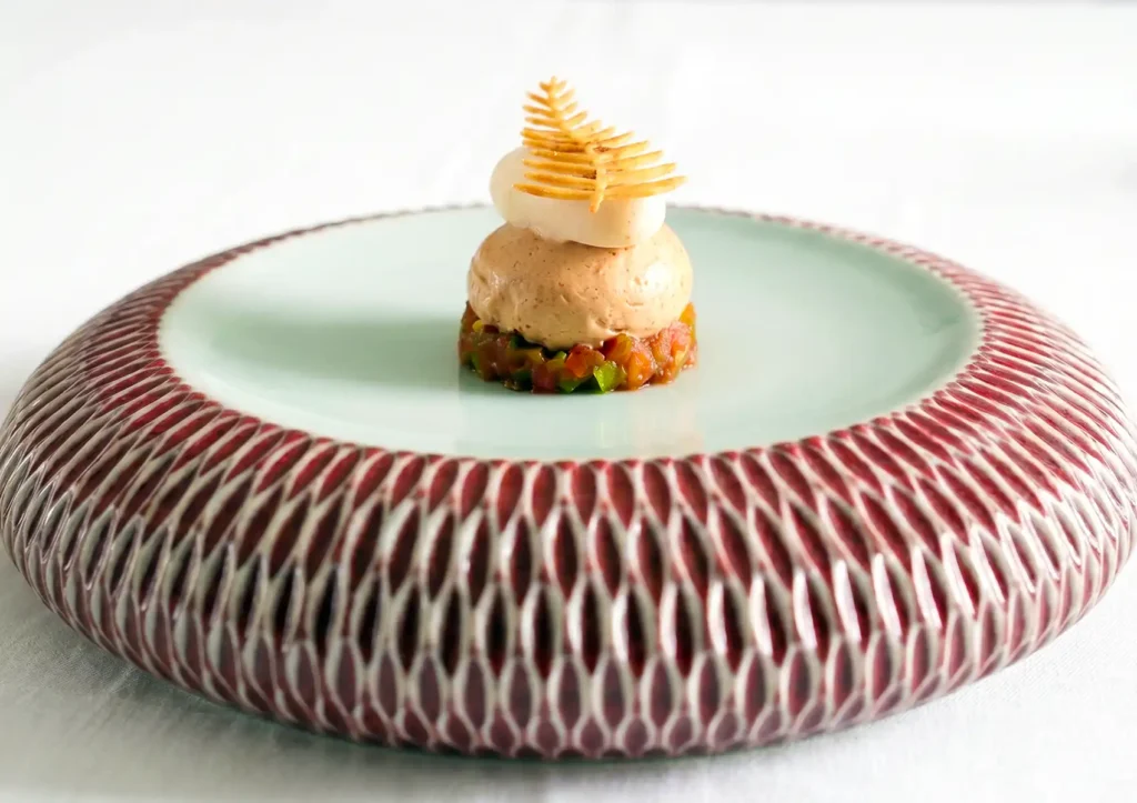 An elegant, multi-layered vegetarian appetizer featuring diced vegetables, a smooth mousse, and a delicate leaf-shaped crisp served on a textured ceramic plate, representing fine dining ubud.