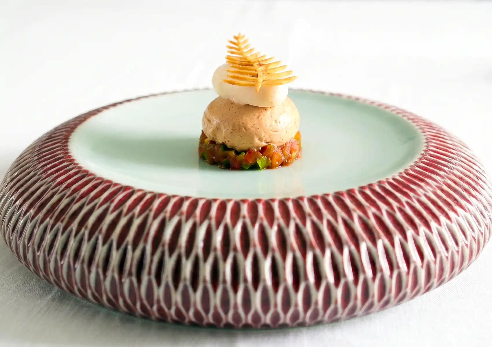An elegant, multi-layered vegetarian appetizer featuring diced vegetables, a smooth mousse, and a delicate leaf-shaped crisp served on a textured ceramic plate, representing fine dining ubud.