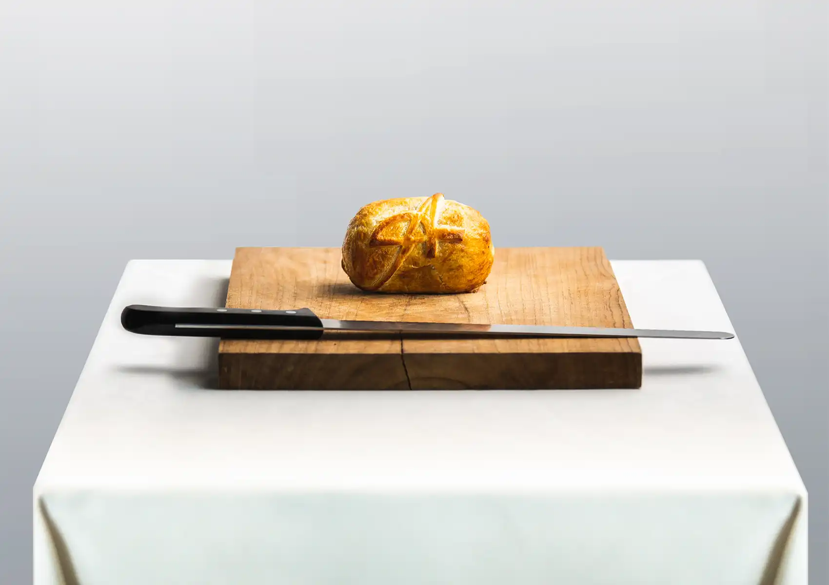 A perfectly baked venison Wellington resting on a wooden carving board next to a long knife, highlighting the exquisite presentation of fine dining Bali.