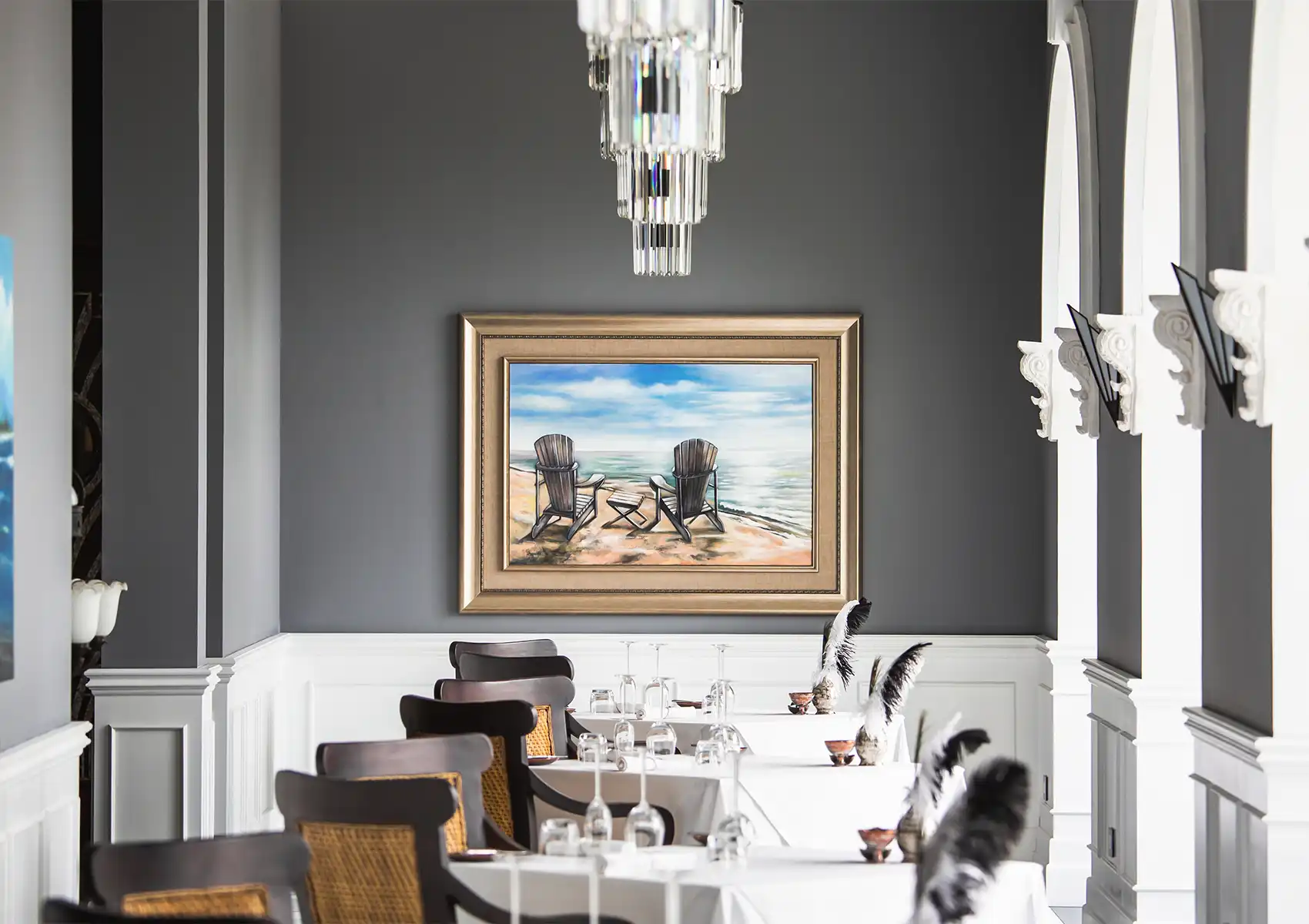 An elegant dining room featuring a crystal chandelier, a framed beach painting, and perfectly set tables ready for fine dining bali.
